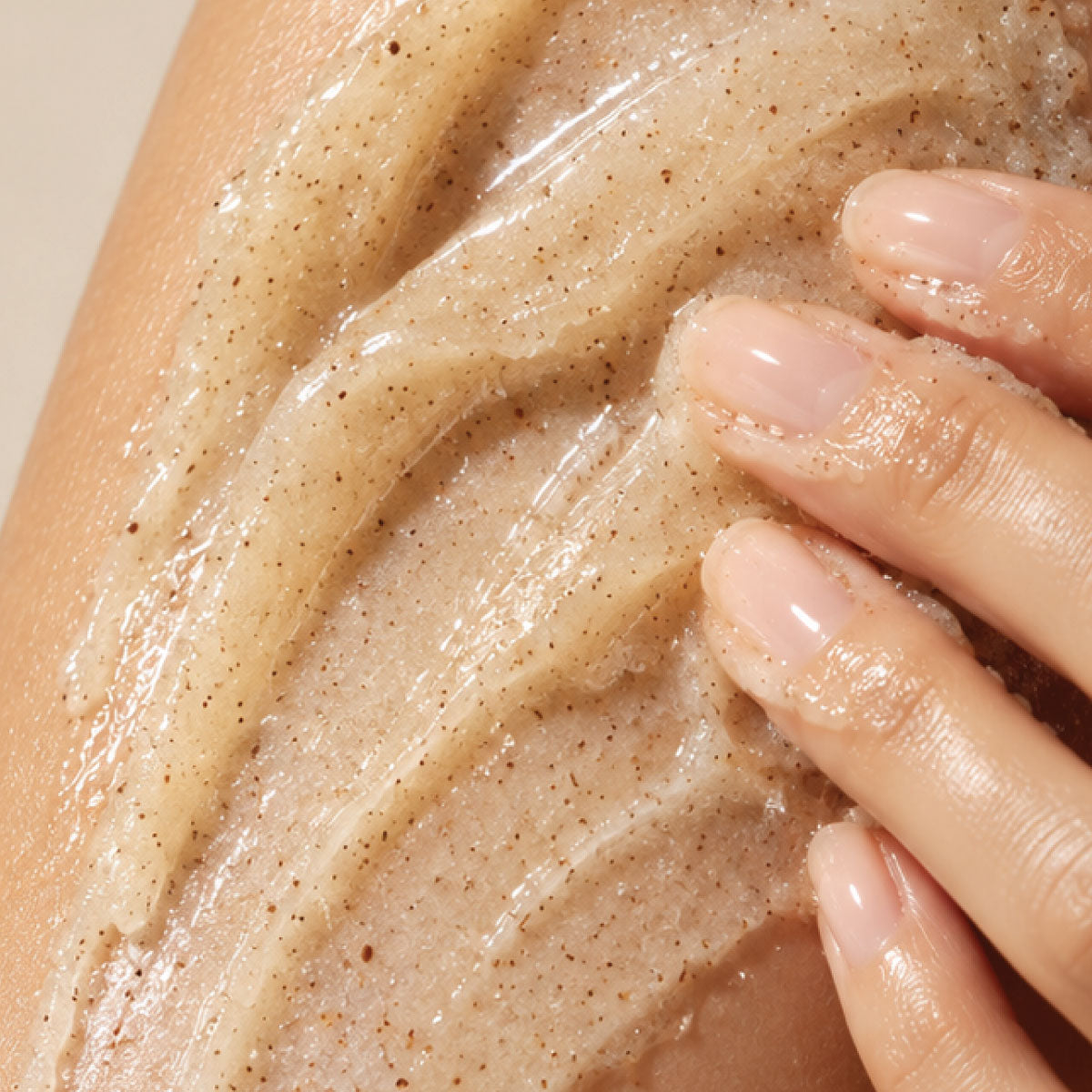 Close-up of fingers massaging a creamy body scrub with fine exfoliating particles onto wet skin.