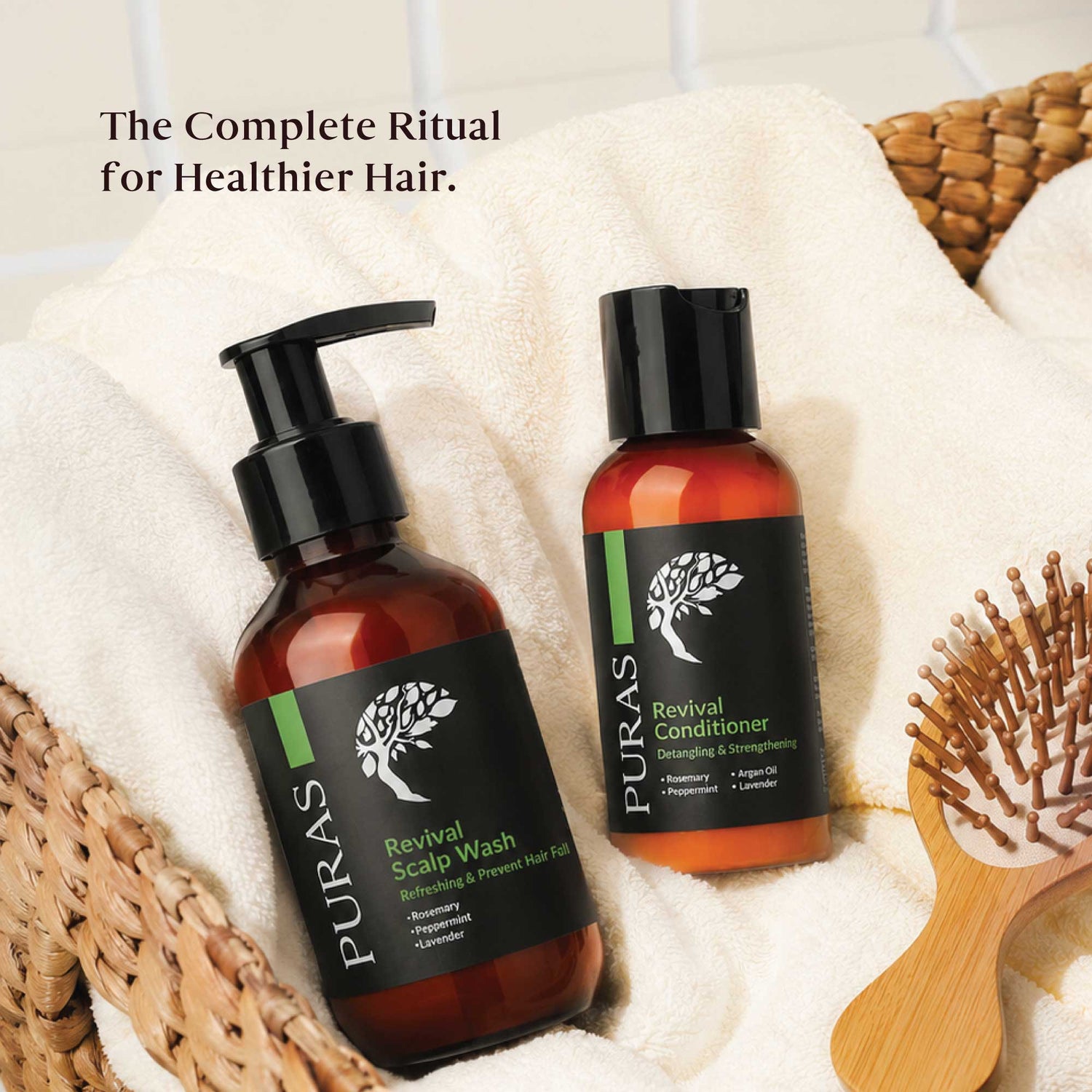 Two PURAS hair care bottles, Revival Scalp Wash and Revival Conditioner, displayed on white towels with a wooden hairbrush and woven baskets in the background. Text at the top reads 'The Complete Ritual for Healthier Hair.
