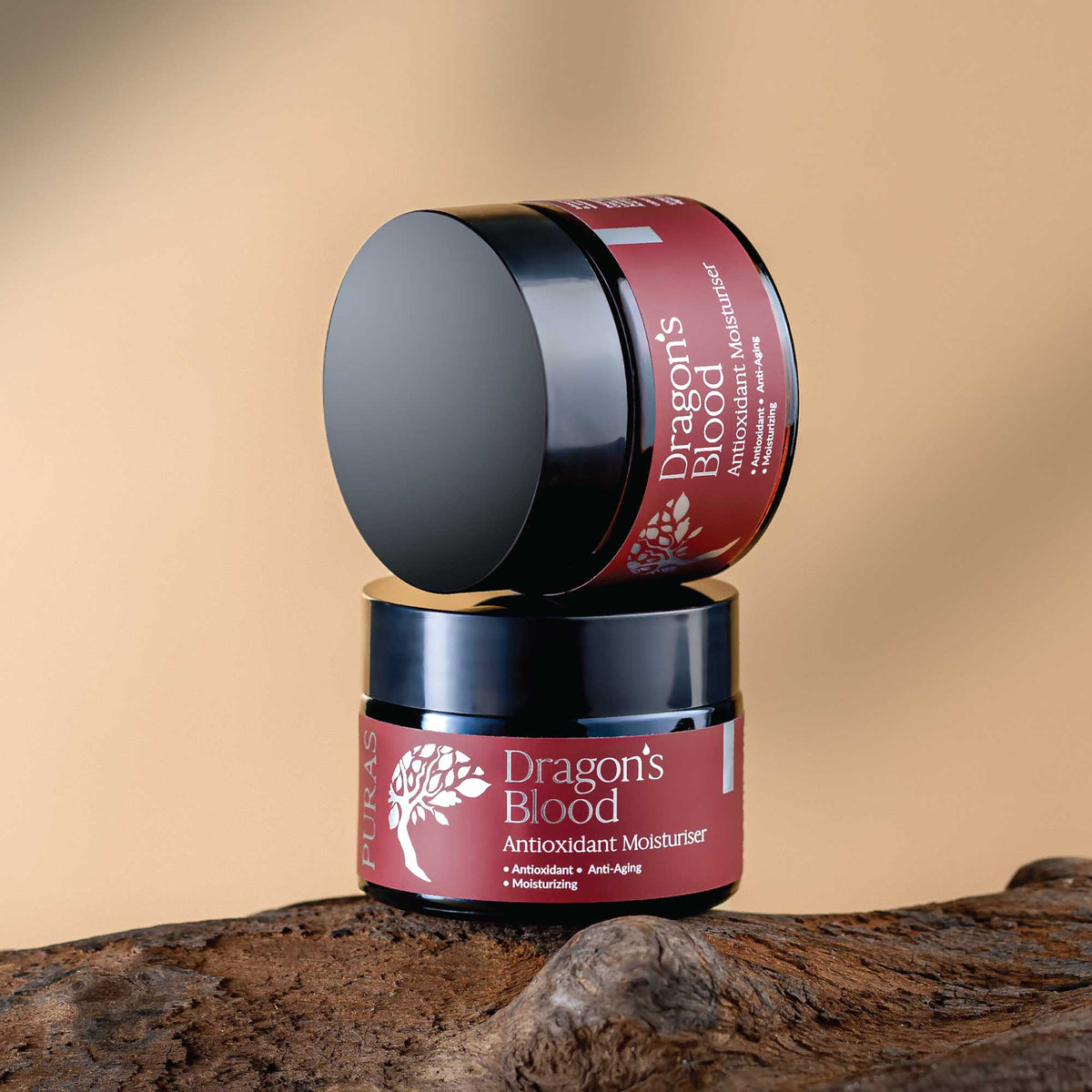 Two jars of 'Dragon's Blood' Antioxidant Moisturizer on a wooden surface with a beige background.