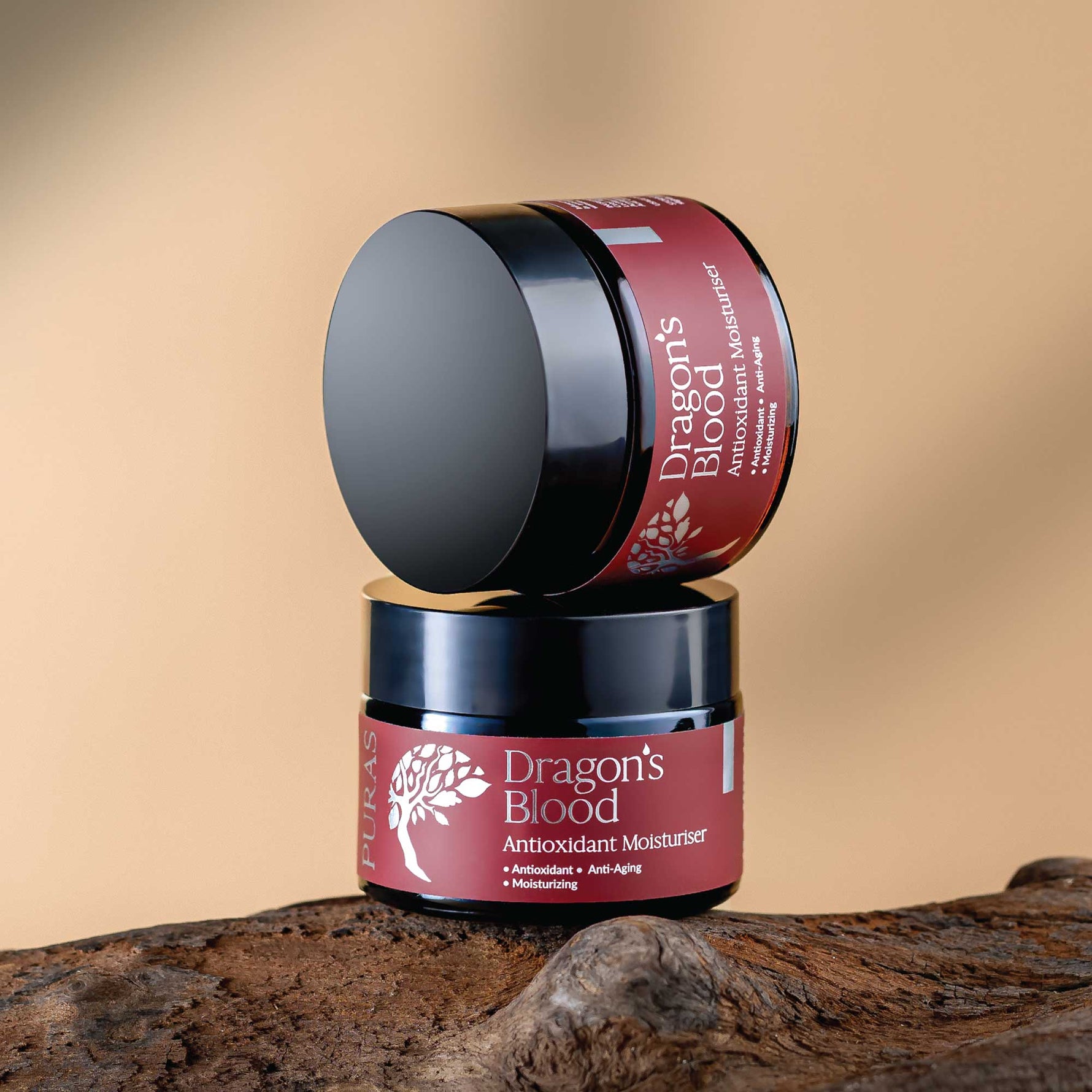 Two jars of 'Dragon's Blood' Antioxidant Moisturizer on a wooden surface with a beige background.