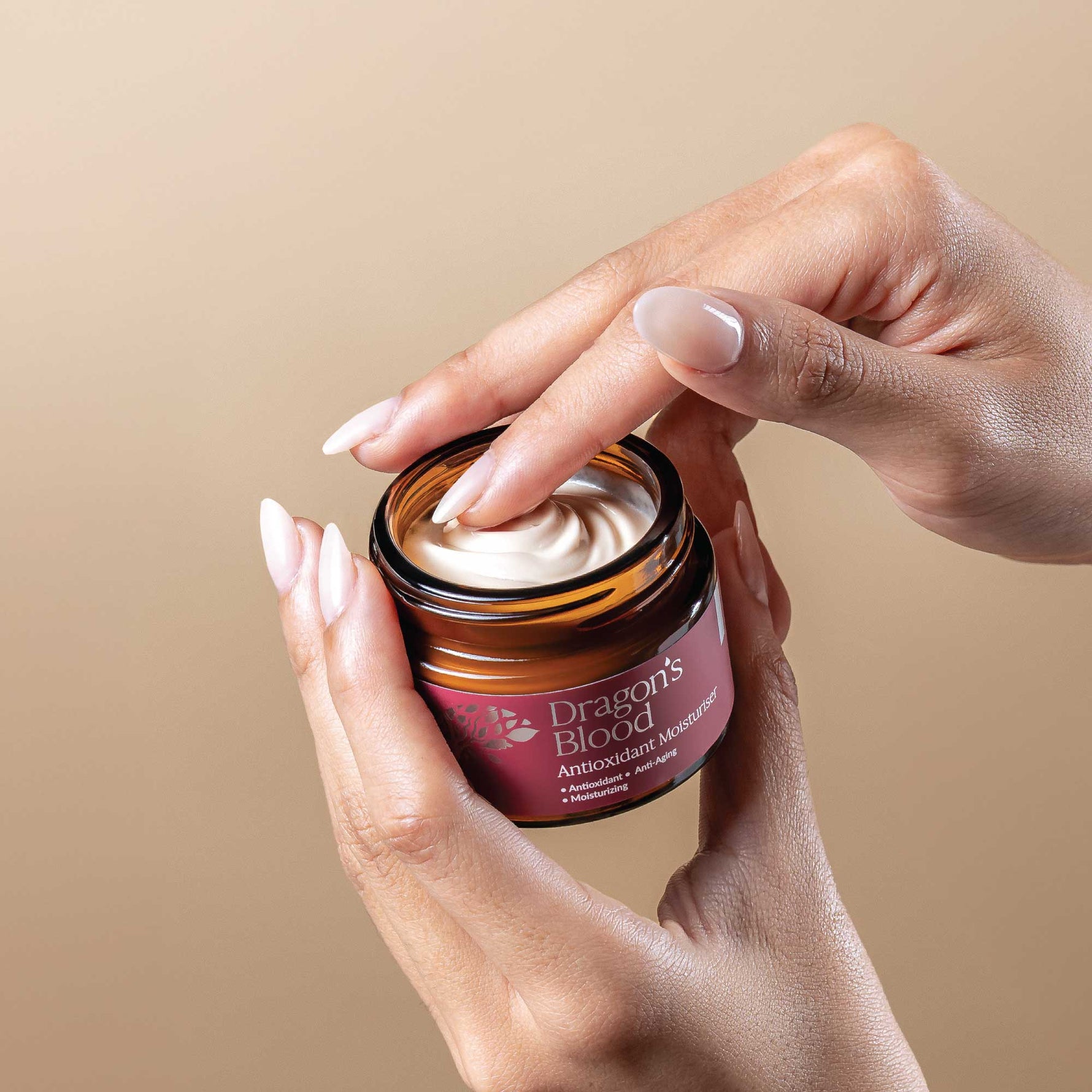 Hand applying cream from a jar labeled 'Dragon's Blood' against a beige background