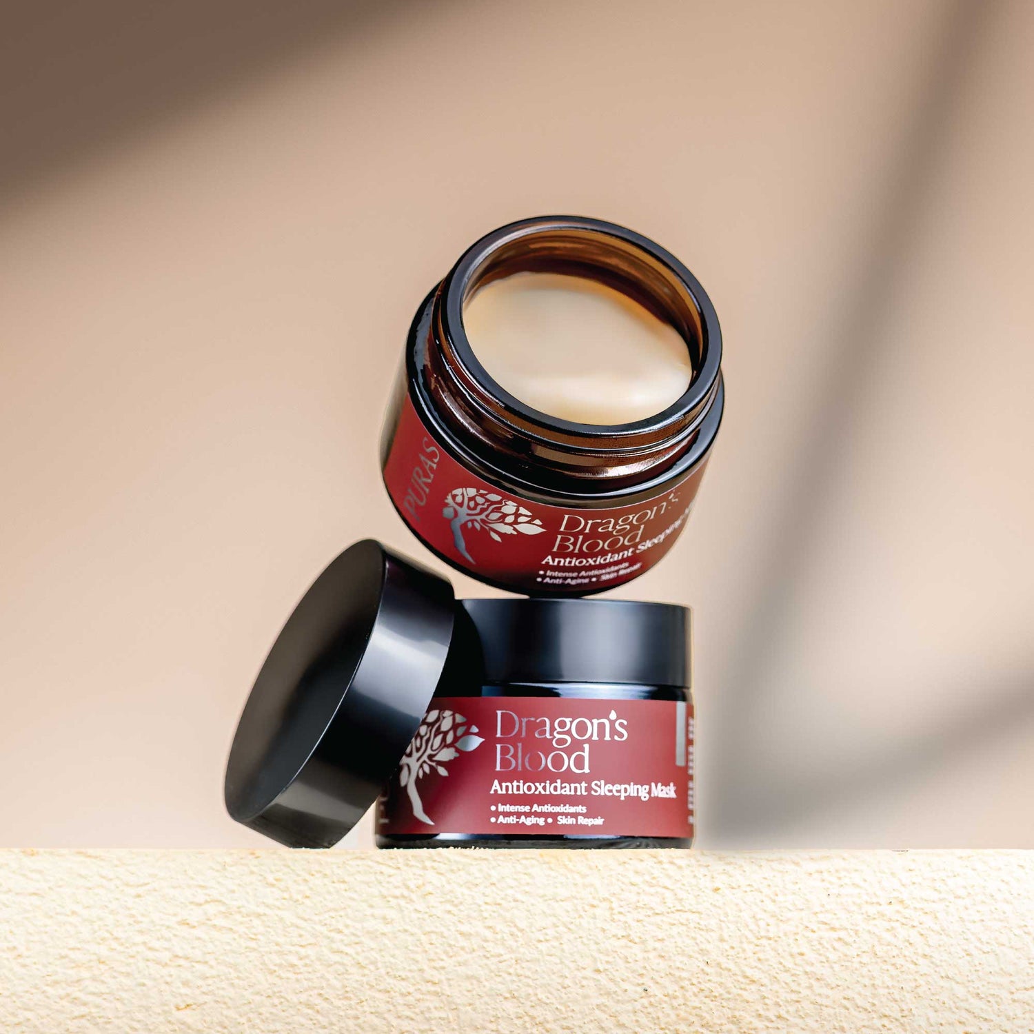 Two jars of 'Dragon's Blood' antioxidant sleeping mask on a beige background