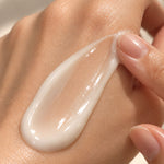 A close-up of a glossy, thick cream or lotion swirled on skin, with a finger gently touching the edge of the smear.