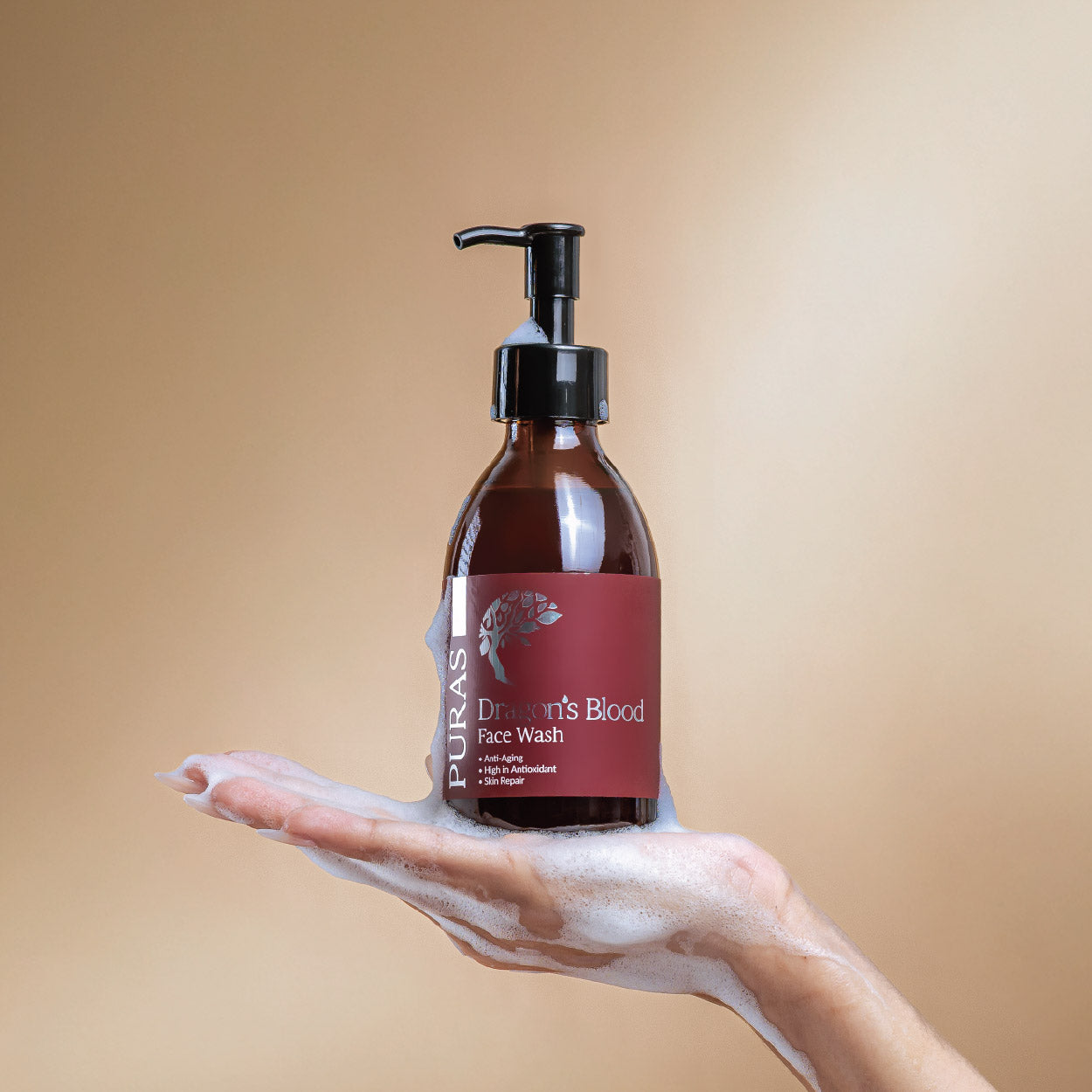 Bottle of Puras Dragon's Blood Face Wash with a hand holding foam on a beige background