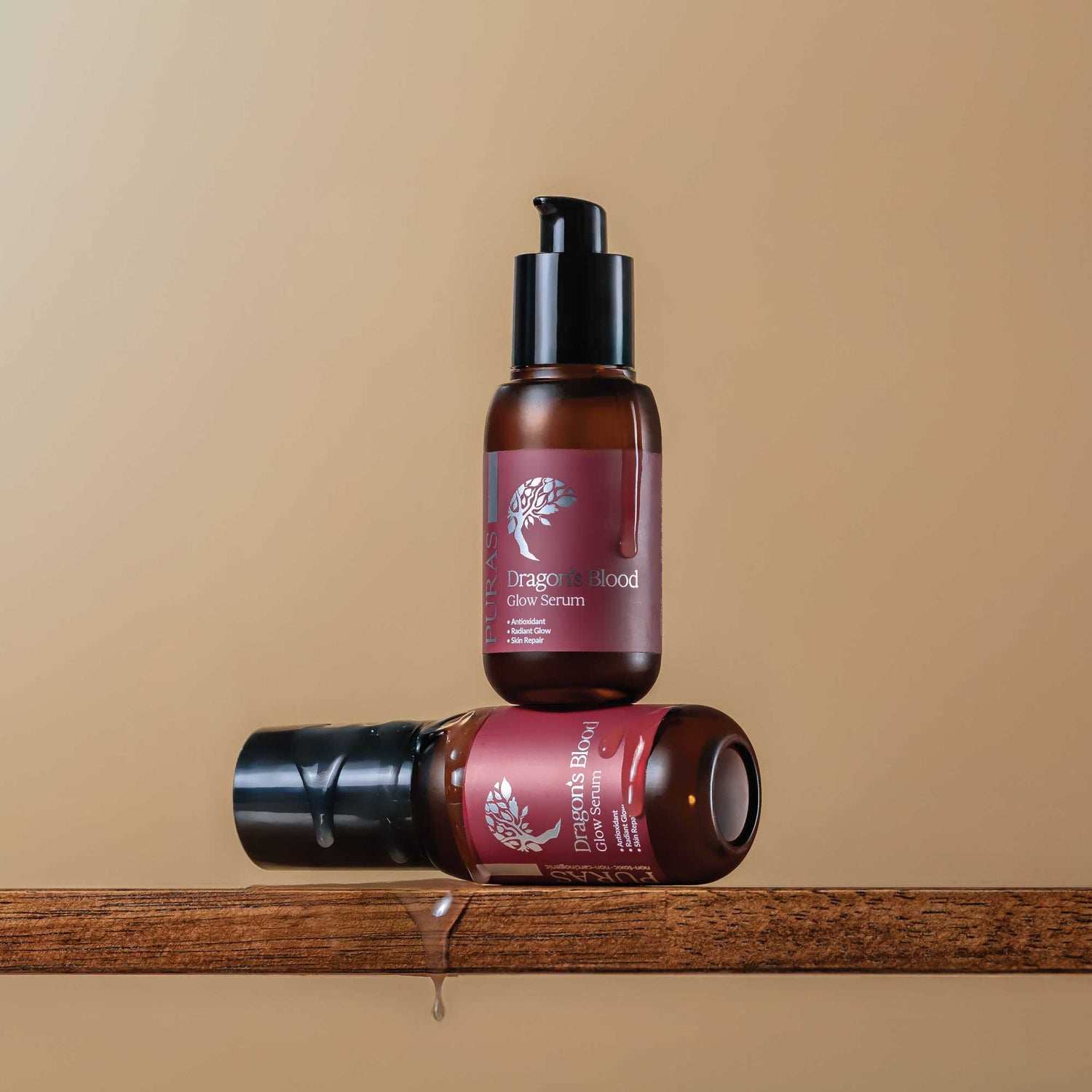 Two bottles of Dragon's Blood serum flowing down the bottle on a wooden surface with a beige background