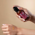 Hand holding a bottle of Puras Glow Serum product with the serum texture on a hand in a beige background