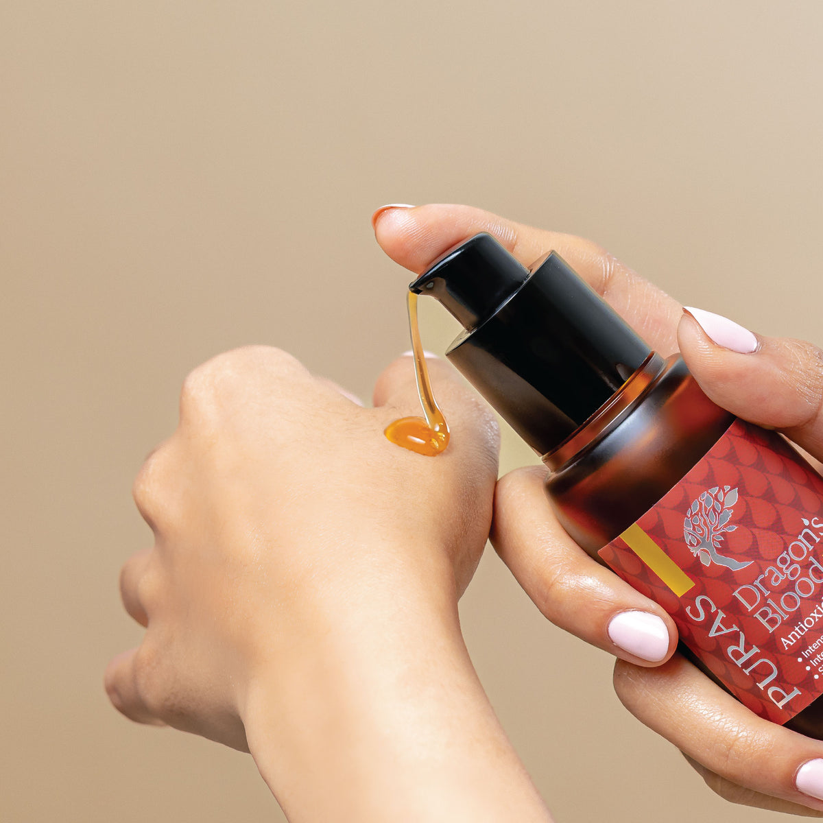 Hand holding a bottle of Dragon Blood peptide glow serum with pump and serum texture on hand in beige background