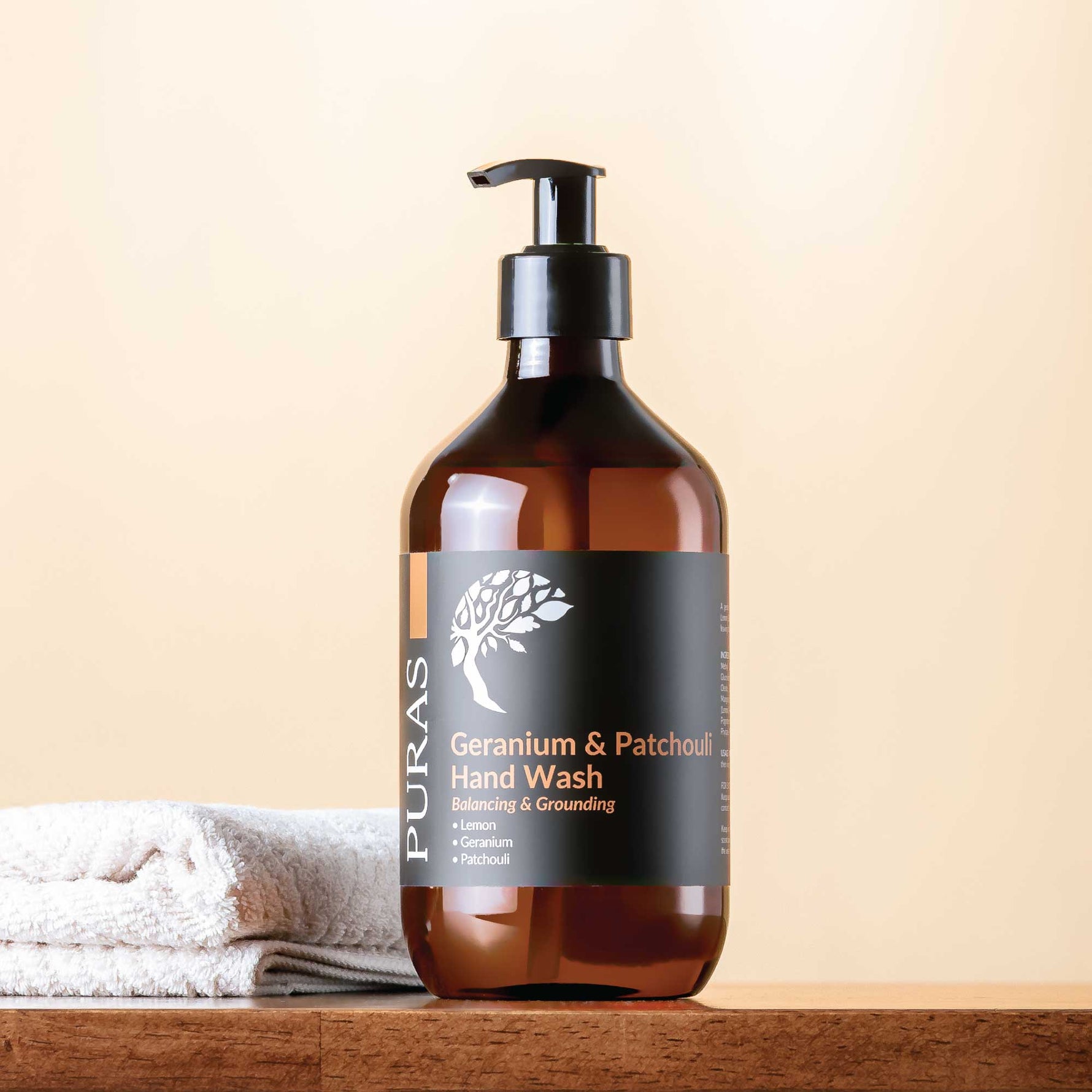 Brown bottle of Puras Geranium & Patchouli Hand Wash on a wooden surface with a beige background