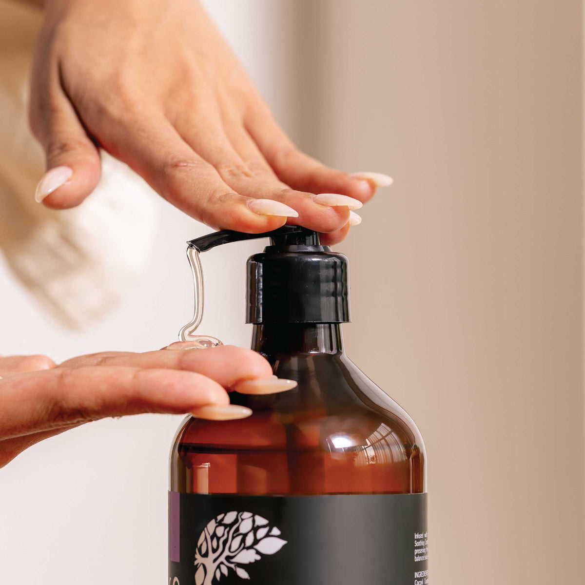 Person holding a brown bottle with a black pump against a neutral background