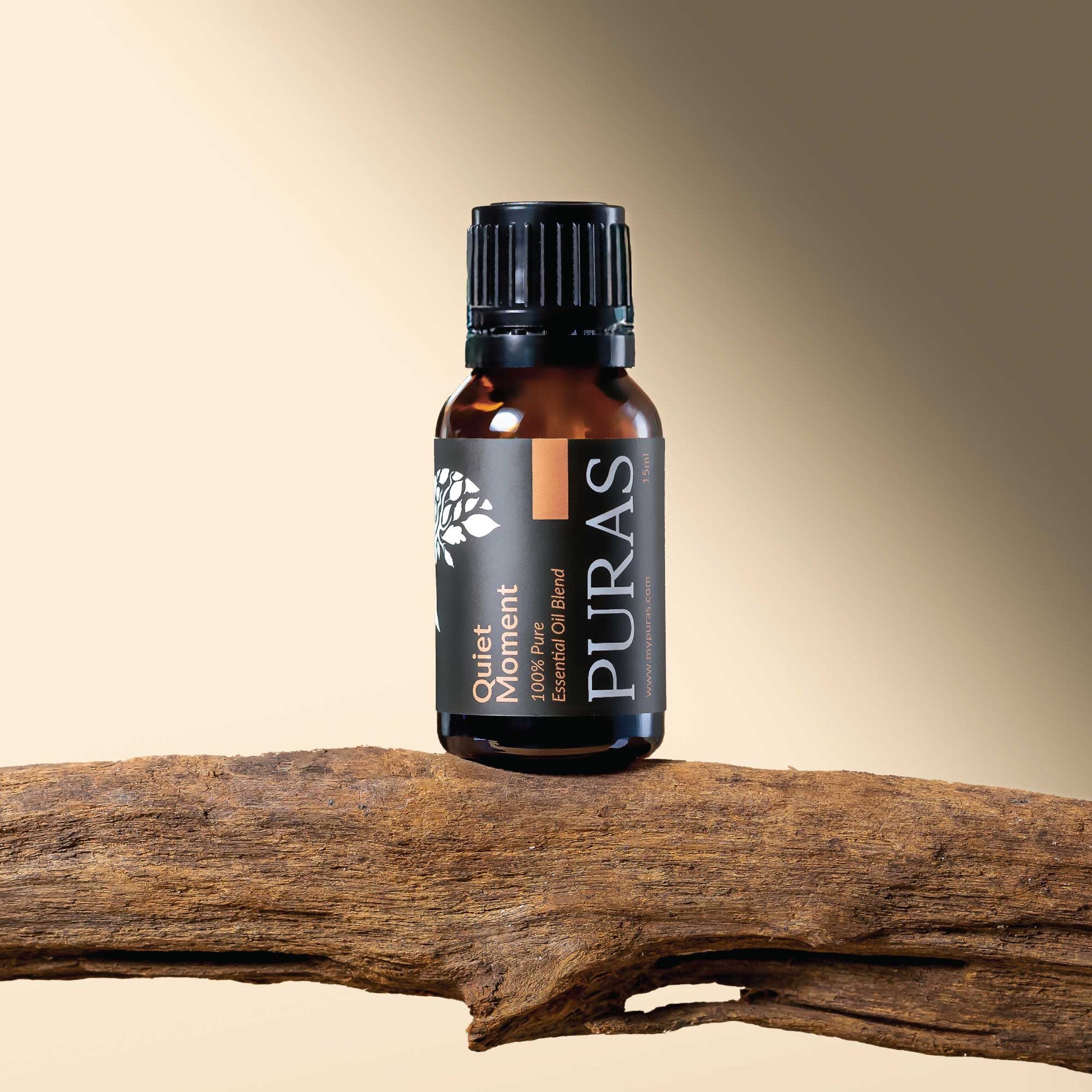 Puras "Quiet Moment" essential oil bottle on a wooden branch with a gradient beige background