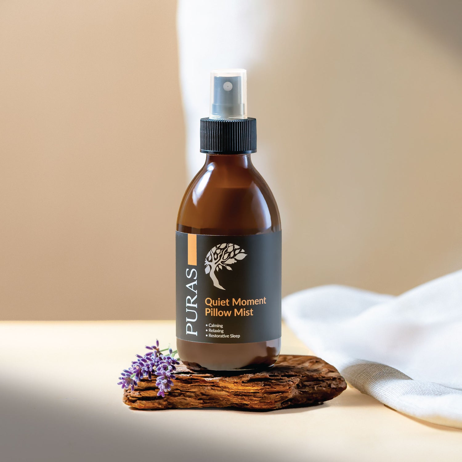 Puras Quiet Moment Pillow Mist bottle on a wooden coaster with lavender flowers and white fabric in the background.