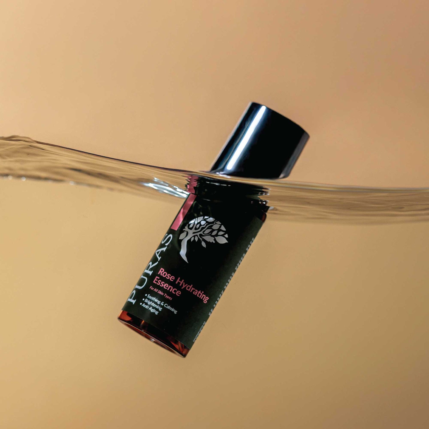 Rose Hydrating Essence bottle with black cap floating in water on a beige background